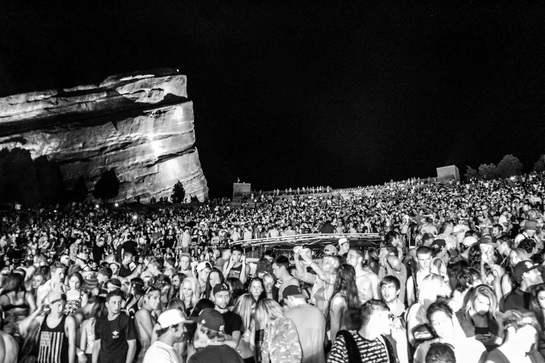 Black-and-white photo of a dense crowd at Red Rocks at night, with a huge floodlit rock towering above them.