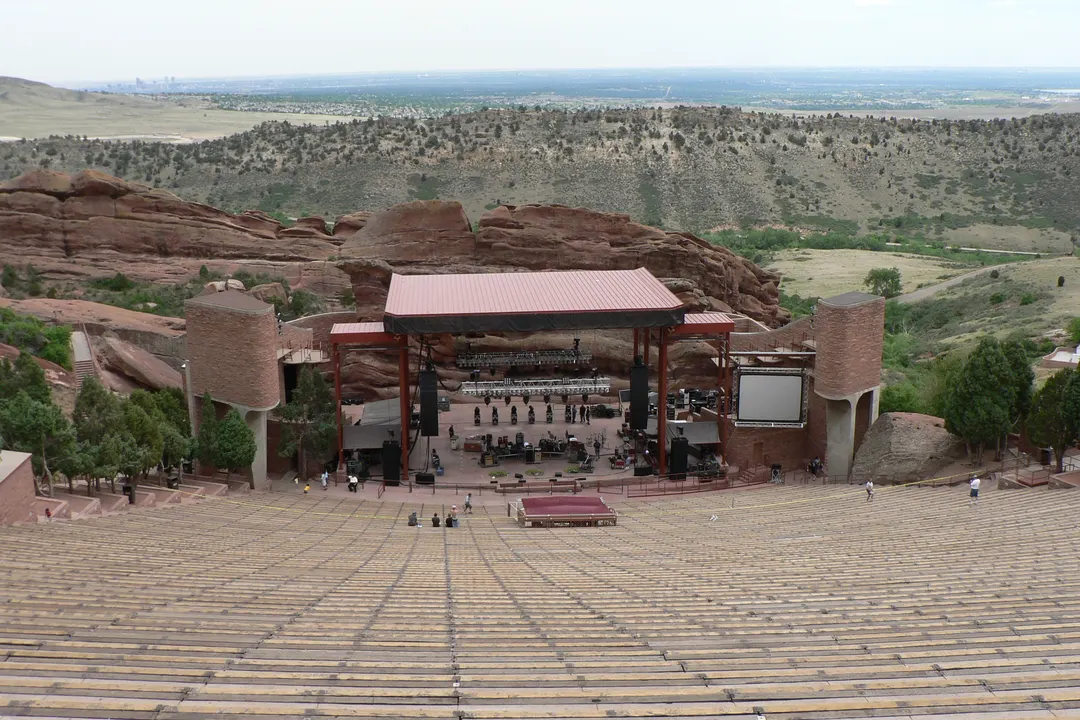 The empty amphitheatre at Red Rocks: rows of benches running down to the stage, framed by red rock formations, with green plains stretching to the horizon.