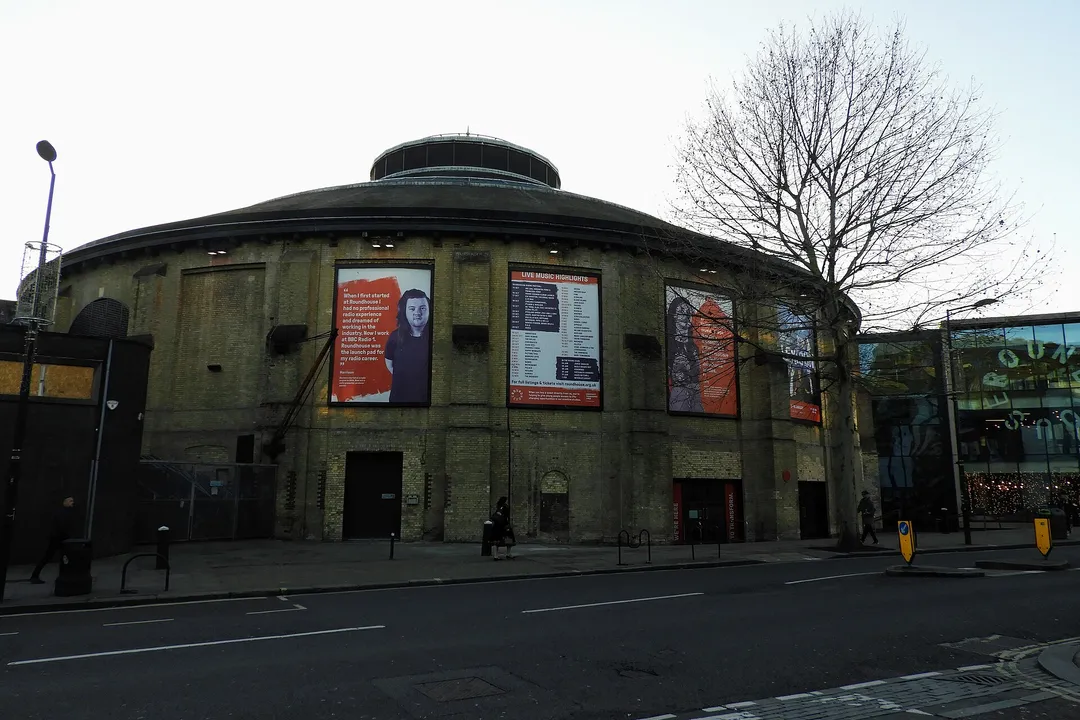 The Roundhouse from Chalk Farm Road: the round brick building with its low conical roof and central lantern, with show posters on its walls.